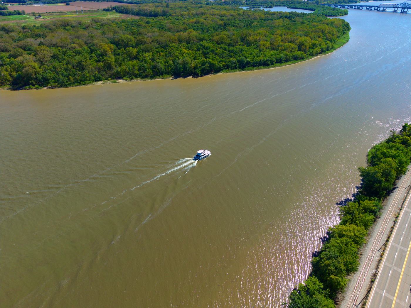 Boat cruising the Illinois River with a bridge in the distance, aerial view